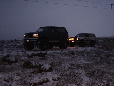 1996 Ford Bronco - Two SUVs are parked on a snowy, rocky landscape under a dark sky.