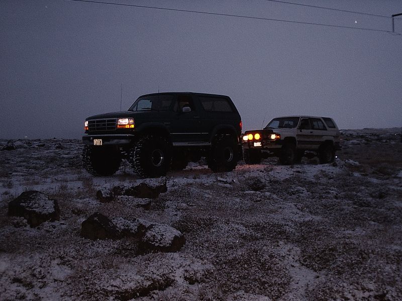 Green lifted Ford Bronco and white Toyota 4Runner on snowy rocky ground at dusk