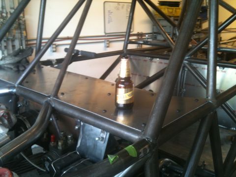 1966 Ford Bronco - A beer bottle rests on the metal floor of a custom-built vehicle chassis in a workshop setting.