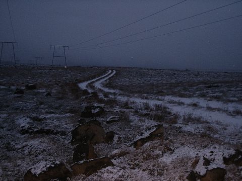 1996 Ford Bronco - A desolate, snow-dusted landscape stretches out under a twilight sky, marked by a winding dirt track and tall power line towers.