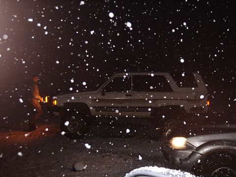 1996 Ford Bronco - A white SUV and another vehicle are visible in falling snow at night.