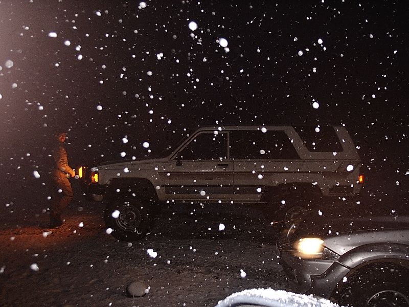 Light SUV in profile at night during heavy snowfall with person nearby