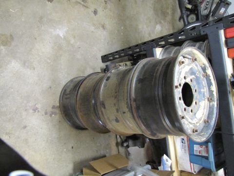 1995 Ford Bronco - Several used truck wheels are stacked on a concrete floor next to a metal shelf.