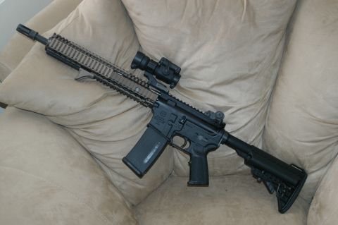 1996 Ford Bronco - An AR-15 style rifle, equipped with a red dot sight and a tan handguard, rests on a cushioned surface.
