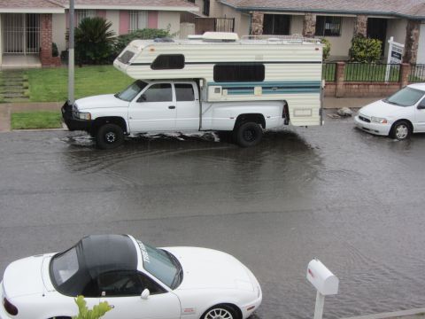 1968 Ford Mustang - A white pickup truck with a camper shell navigates a flooded street, with two other cars visible.