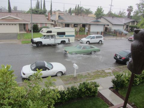 1968 Ford Mustang - Multiple vehicles navigate a flooded suburban street during heavy rain.