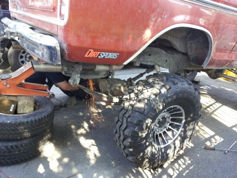 1978 Ford Bronco - A mechanic works on the rear axle of a red Ford Bronco, cutting a leaf spring with sparks flying.