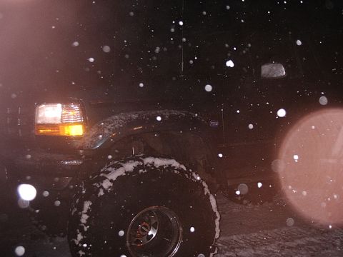 1996 Ford Bronco - A Ford Bronco is parked outside during a snowfall at night, with snow accumulating on its tires and body.