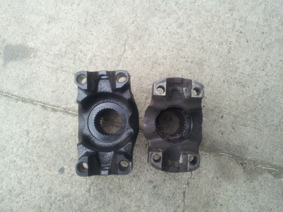 Two driveshaft yokes, one new and one used, on a concrete surface