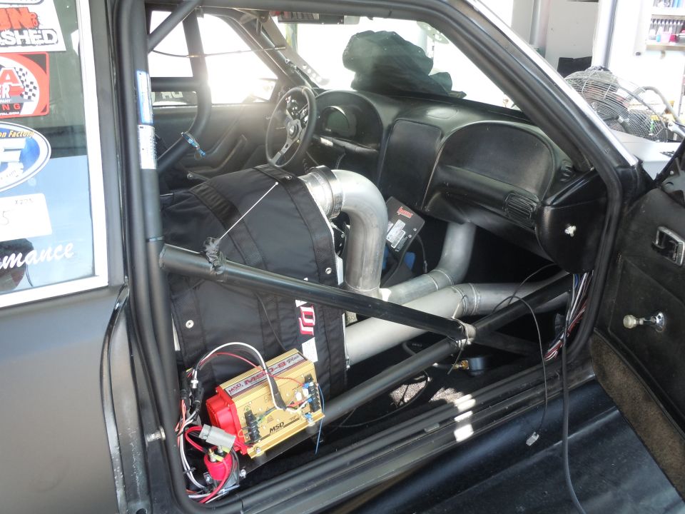 Car interior with roll cage, custom exhaust pipes, and racing seat. A yellow MSD ignition box is visible