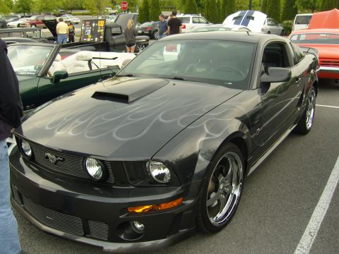 2007 Ford Mustang - A dark gray 2007 Ford Mustang with custom silver flame graphics and a hood scoop is parked at a car show.