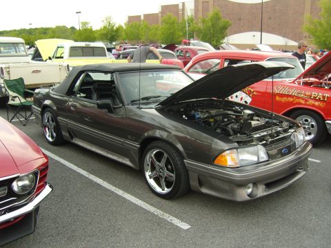 2007 Ford Mustang - A dark gray convertible is parked with its hood open, revealing the engine compartment. Other vehicles are visible in the background.
