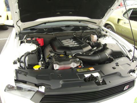 2007 Ford Mustang - Engine bay of a 2007 Ford Mustang, showing the 5.0 engine. A vintage car is visible in the background.