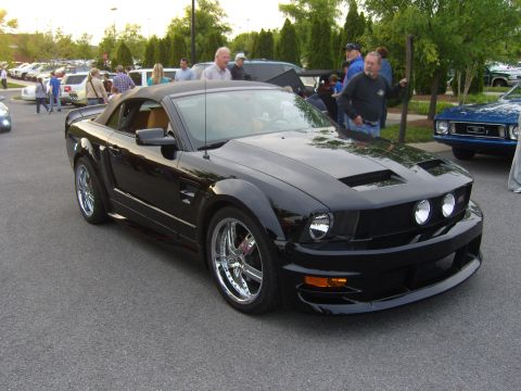 2007 Ford Mustang - A black convertible Ford Mustang is parked on asphalt, with other vehicles and people in the background.