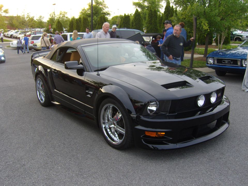 Black convertible Ford Mustang with chrome wheels and hood scoops, viewed from the front three-quarter angle