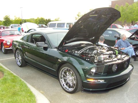 2007 Ford Mustang - Dark green 2007 Ford Mustang on display with hood open, parked next to other vehicles.