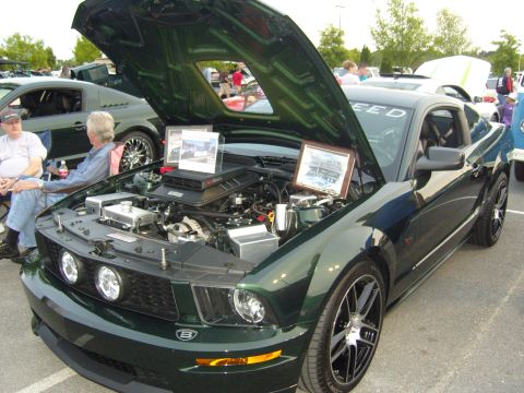 2007 Ford Mustang - A dark green Ford Mustang is displayed with its hood open at a car show, revealing the engine and informational displays.