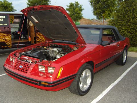 2007 Ford Mustang - Red convertible parked in a lot, hood open to reveal the engine bay.