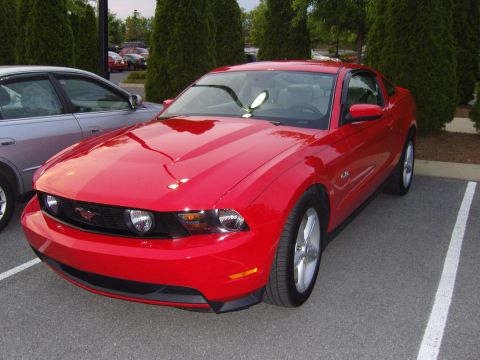 2007 Ford Mustang - A red Ford Mustang is parked in a lot, showing off its racing stripes on the hood.
