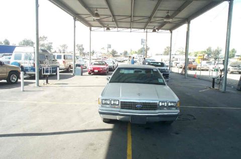 1991 Ford LTD Crown Victoria - A silver sedan is parked under a covered lot with other vehicles visible.