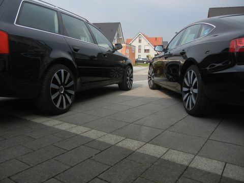 2010 Audi A4 - Two black Audi cars are parked on a paved driveway in front of houses.