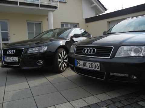 2010 Audi A4 - Two black Audi sedans are parked on a paved driveway in front of a house.