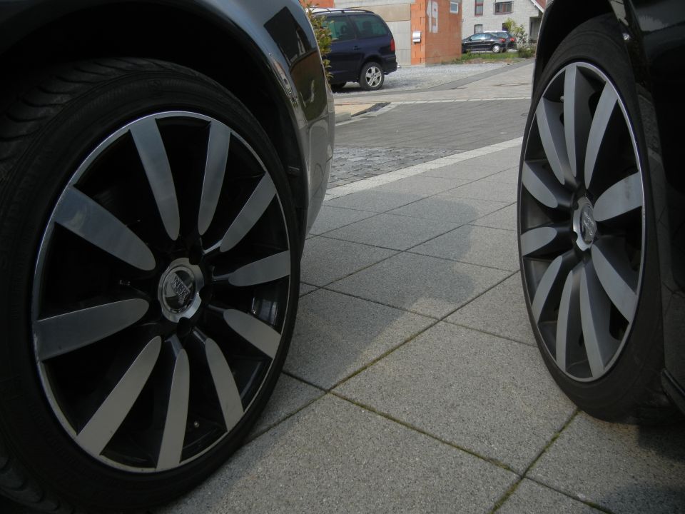 Close-up of two custom alloy wheels with black and silver spokes, parked on a tiled surface
