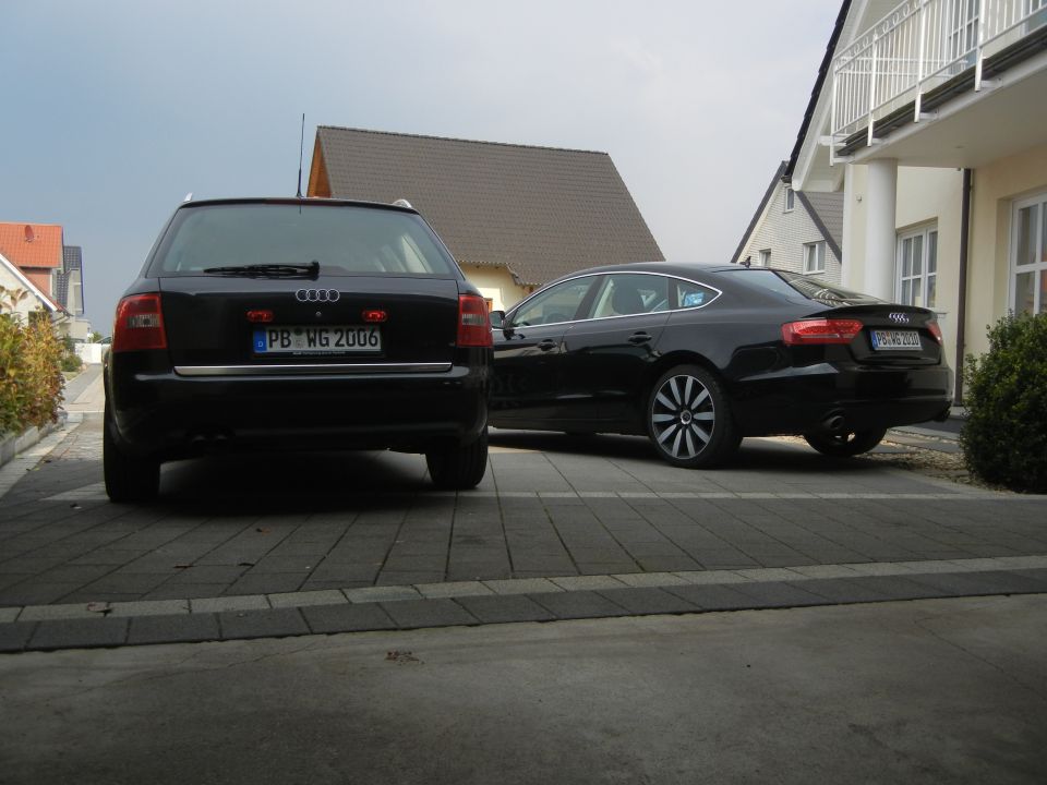 Two black Audi cars parked in a paved courtyard by houses