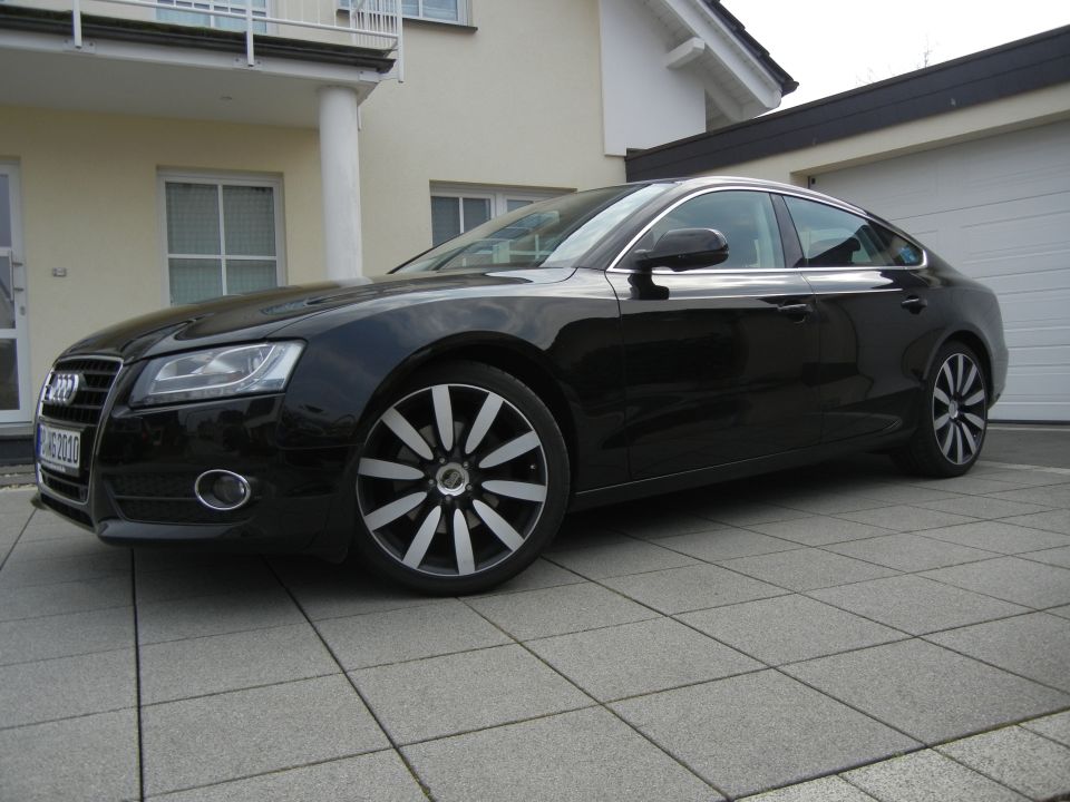Black Audi sedan parked in driveway, front quarter view. License plate reads 'HG 2010'