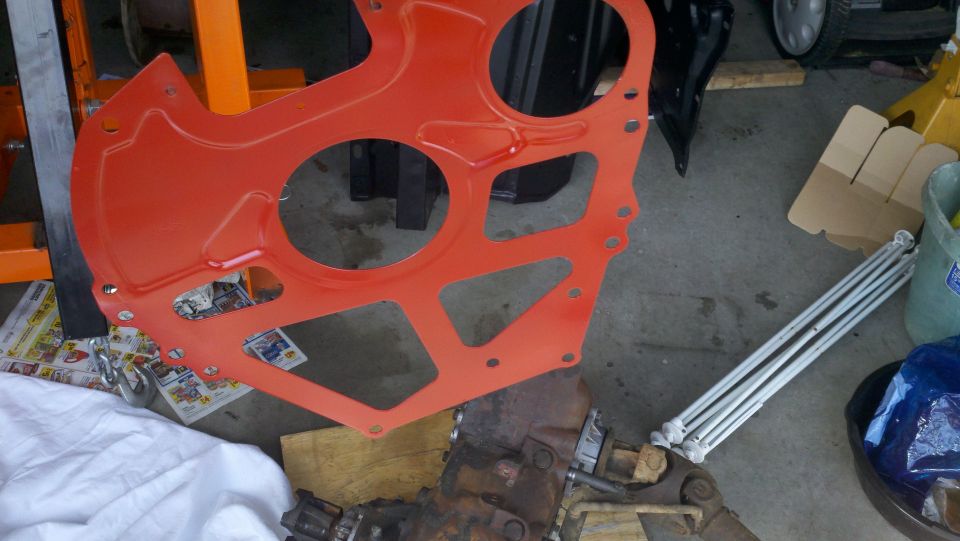 Orange engine plate and transmission on a garage floor with tools and parts around