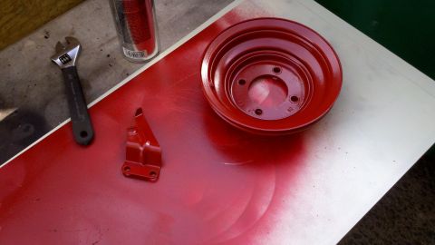 1978 Ford Bronco - A red pulley and bracket are shown after being spray-painted, with a wrench nearby.