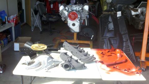 1978 Ford Bronco - Engine and various automotive parts are laid out on a table in a garage.