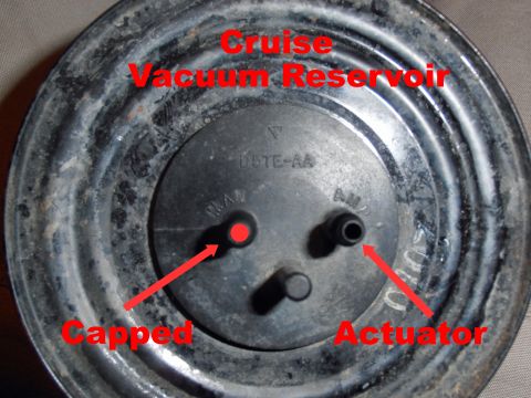 1990 Ford Bronco - Close-up of a round metal cruise control vacuum reservoir stamped 'D5TE-AA', showing two rubber vacuum ports labeled 'MAN' (marked Capped w…