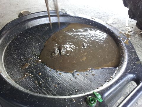 1978 Ford Bronco - Old, sludgy oil is being drained from a vehicle into a catch pan.