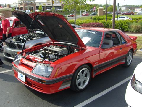 2007 Ford Mustang - A red coupe, identified as a Saleen Mustang by a windshield decal, is displayed with its hood open at a car show.
