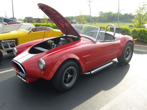 2007 Ford Mustang - A red convertible with its hood open is parked next to a yellow car at a cruise-in.
