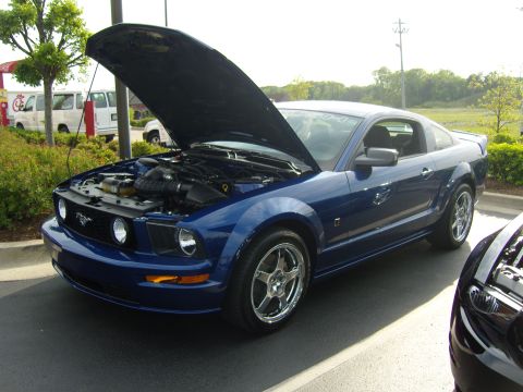2007 Ford Mustang - A blue Ford Mustang is parked with its hood up, revealing the engine compartment. Another vehicle is partially visible in the foreground.
