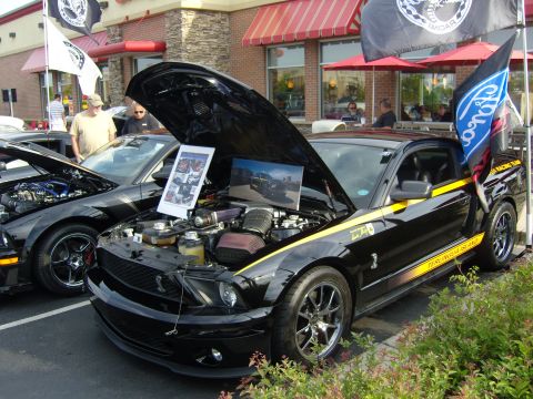 2007 Ford Mustang - A black Ford Mustang with yellow racing stripes is parked with its hood open, showing the engine and display photos.