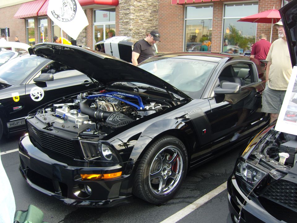 Black 2007 Ford Mustang with hood open, showing engine modifications. Another Mustang is visible to the left