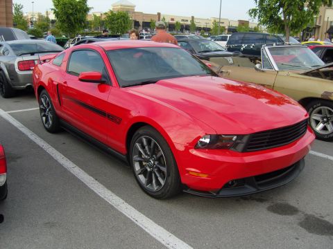 2007 Ford Mustang - A red Ford Mustang is parked in a lot next to other vehicles.