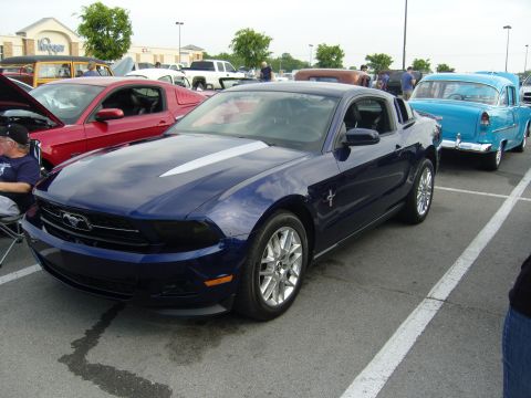 2007 Ford Mustang - A dark blue Ford Mustang with silver racing stripes is parked in a lot during a car show.