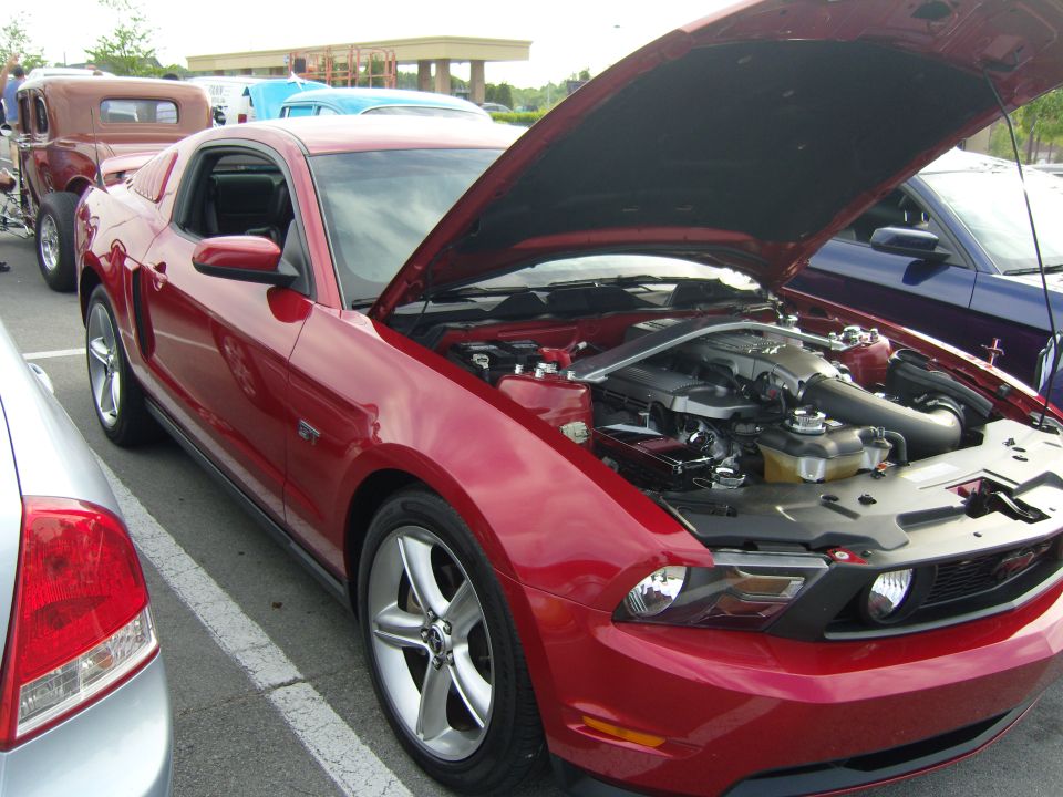 Red Ford Mustang, hood open showing engine. Other cars in background