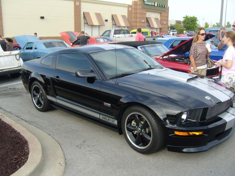 2007 Ford Mustang - A black 2007 Ford Mustang Shelby GT is parked at a car show with other vehicles visible.