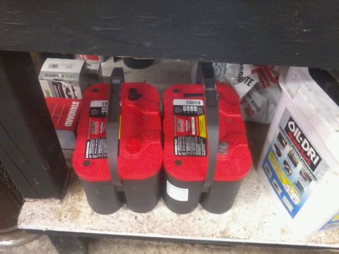 1995 Ford F-150 - Two red Optima batteries are stored on a shelf with other automotive supplies.