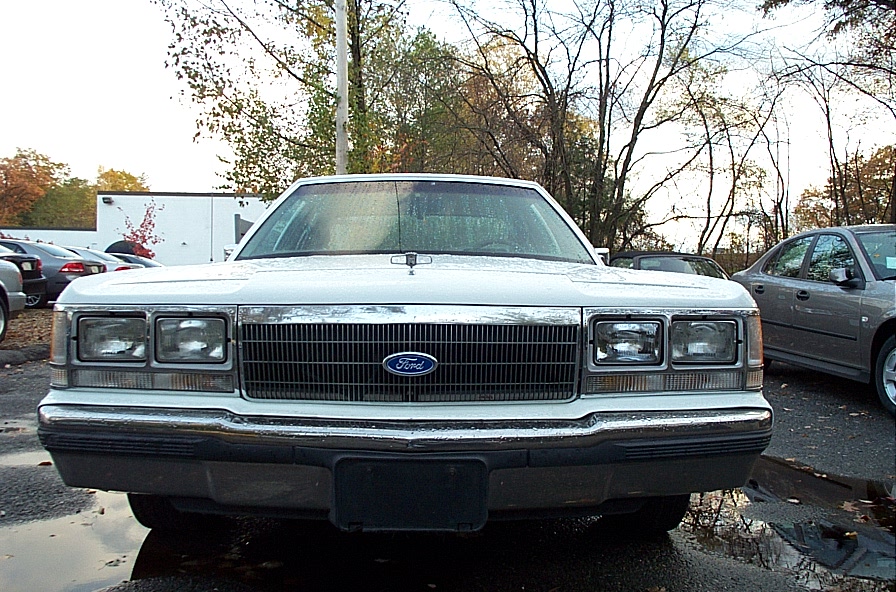 White 1991 Ford Crown Victoria LTD front view, chrome grille with Ford logo, dual headlights, wet pavement