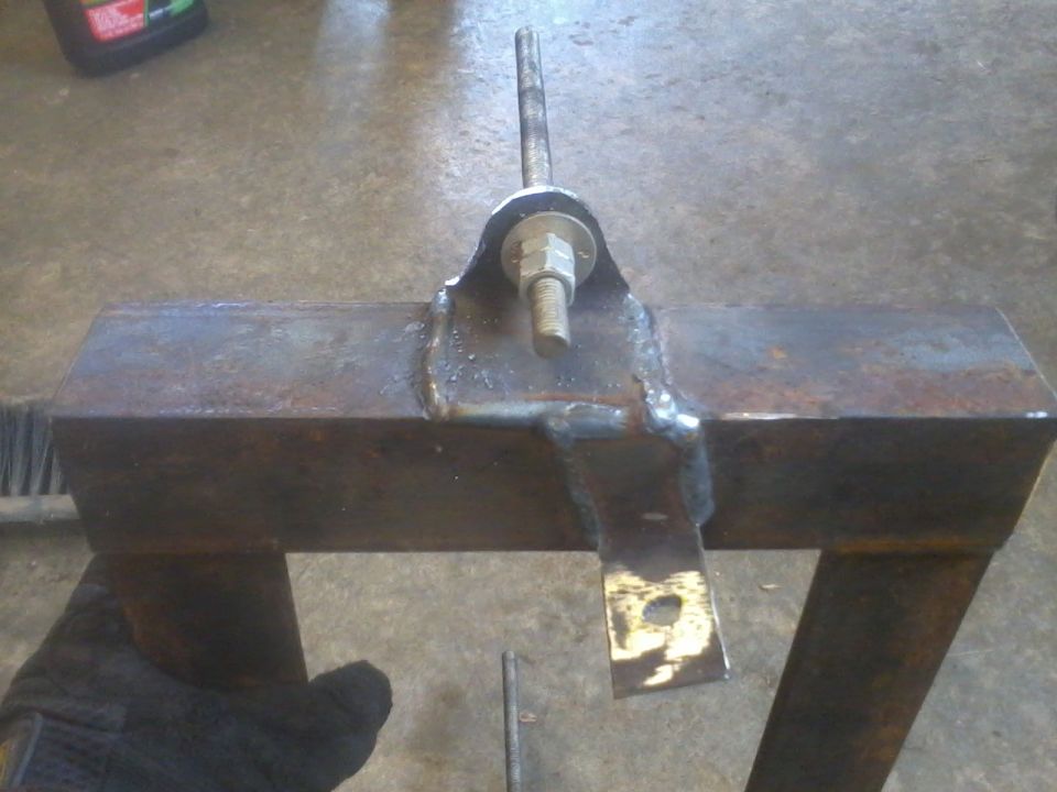 Welded metal bracket with a bolt and nut assembly. A hand in a black glove is visible
