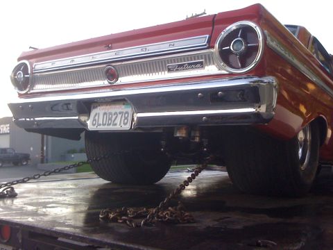 1964 Ford Ranchero - A red 1964 Ford Falcon Futura is chained to a flatbed trailer, viewed from the rear.