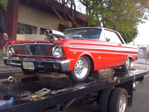 1964 Ford Ranchero - A red 1964 Ford Falcon with a prominent hood scoop is loaded onto a flatbed tow truck.