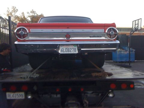 1964 Ford Ranchero - The rear of a red Falcon is secured with chains to a flatbed tow truck.