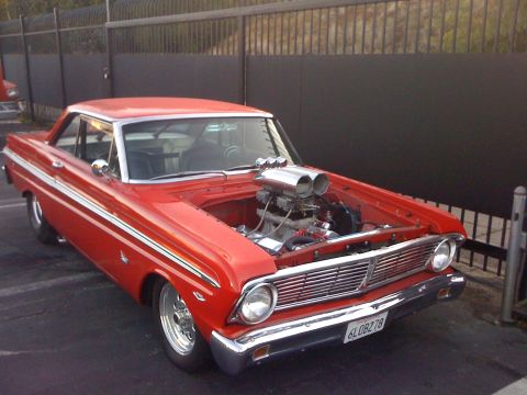 1964 Ford Ranchero - This red coupe features a prominent dual carburetor setup under its open hood, with a distinctive body style.